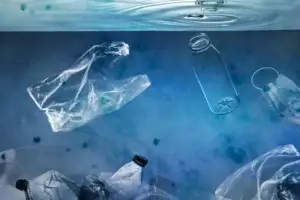 Various pieces of clear and white plastic waste, including bags and bottles, floating and submerged in murky blue water, illustrating plastic waste in the ocean.